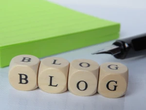 Drvene kockice sa natpisom BLOG, zelenom sveskom i naliv perom u pozadini.